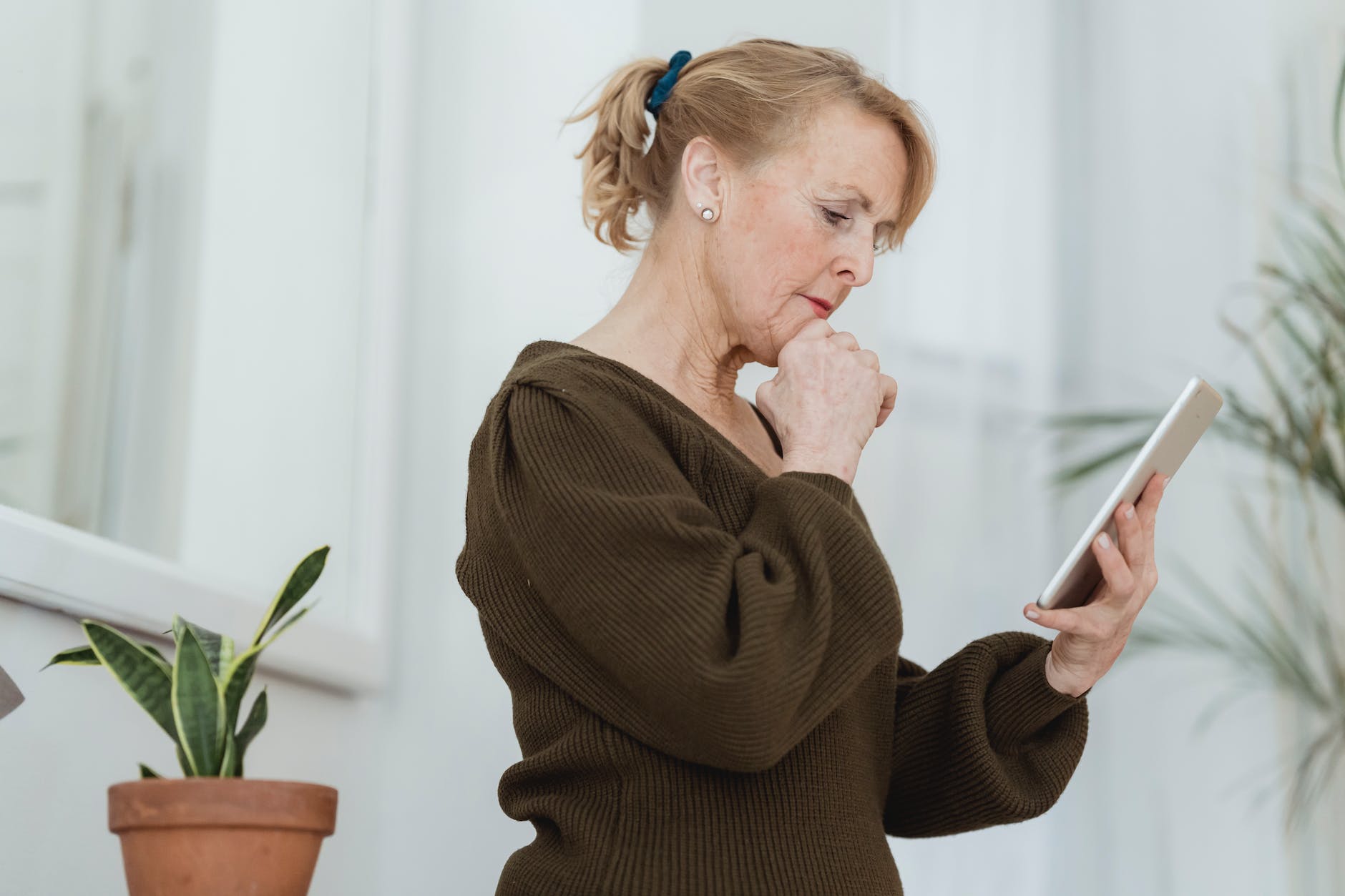 pensive senior woman with smartphone at home