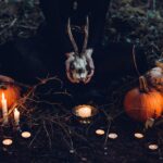 person holding cattle skull surrounded by squash and candles