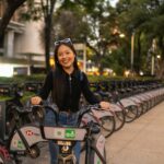 A smiling woman stands by a row of rental bicycles