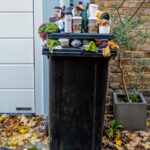 An overflowing black plastic trash bin filled with coffee cups and plastic bags